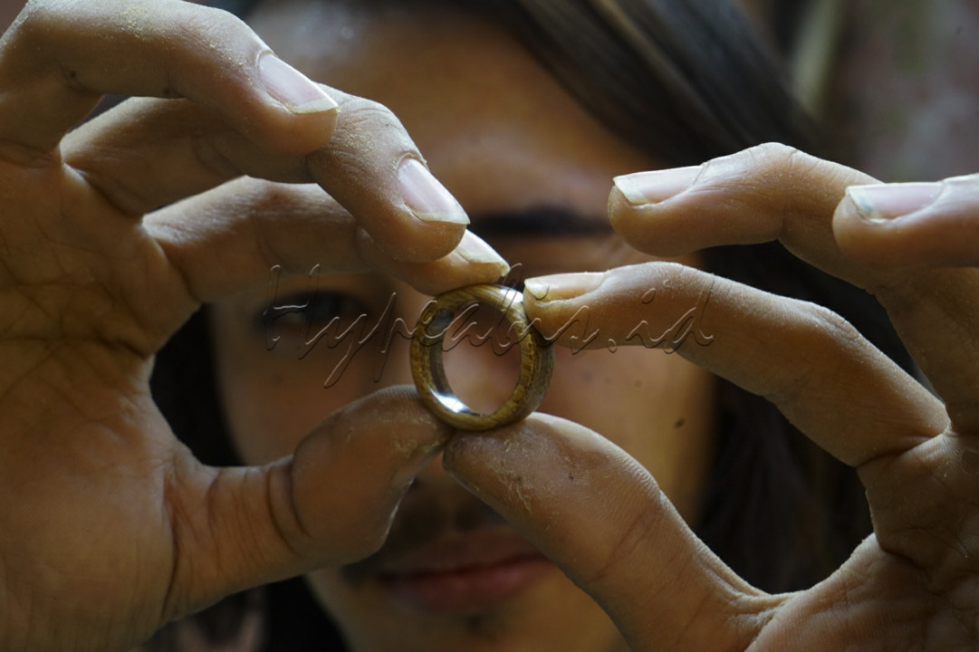 Mohamad Rahman, 28, menyelesaikan pembuatan cincin di studio produksi Indonesian Bamboo Community (IBC), Jalan Melong Asih, Kota Cimahi. Produksi aksesoris ini mengandalkan bahan baku limbah bambu dan kayu dari produksi alat musik yang dihasilkan di IBC. Semula IBC memproduksi alat musik berbahan bambu, namun saat pandemi produksi dialihkan seiring menurunnya permintaan alat musik bambu. <br />
<br />
Setahun lalu Rahman mulai mengembangkan produksi aksesoris dengan material bambu apus atau bambu tali, kayu jati, hingga memakai potongan senar gitar bahkan pecahan kerang sebagai material pelengkap. Dalam satu hari, Rahman bisa memproduksi sebanyak 8 hingga 10 cincin. Dibanderol dengan harga Rp 100 ribu hingga Rp 150 ribu cincin buatan Rahman ini mulanya hanya dijual di lingkungan komunitas dan pertemanan. Saat ini, penjualan cincin yang dikerjakan secara hand made tersebut dipasarkan melalui media sosial instagram<br />
