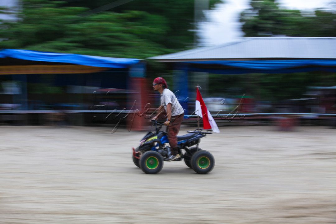 Seorang pria tengah bermain motor ATV sambil membawa bendera merah putih yang merupakan simbol negara Indonsia di pasir putih lumban bul-bul, Balige, Toba, Sumatera Utara. 