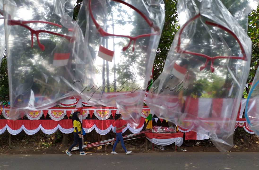 Dua wanita melintas dekat berbagai rupa Bendera Merah Putih serta asoseris Merah Putih lainnya dalam rangka menyambut HUT Kemerdekaanke-75 yang digelar oleh pedagang di tepi jalan di Jl. Raya Bogor, Cibinong - Kabupaten Bogor, Jawa Barat (Senin, 10 Agustus 2020). Selain menjual Bendera Merah Putih serta asoseris kemerdekaan lainnya, para pedagang musiman ini yang tetap berjualan dimasa Pandemi COVID-19 yang belum reda, juga menjual Face Shield bernuansakan Merah Putih dimana Face Shield dapat dipakai oleh siapa saja jika tidak memakai masker.