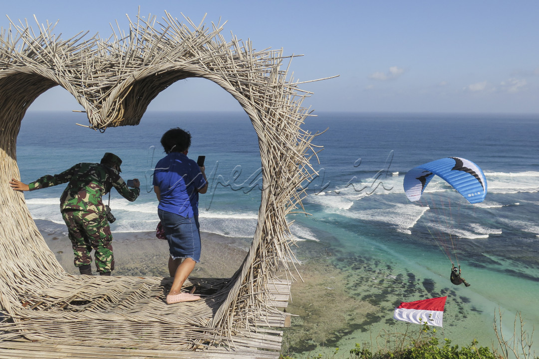 Anggota TNI bersama warga mendokumentasikan seorang anggota TNI lainya yang sedang terbang Paralayang dengan membawa bendera Merah Putih diatas pantai bukit Timbis, Nusa Dua, Bali pada 7 Juli 2020. Kegiatan tersebut merupakan rangkaian latihan bersama jelang perayaan Hari Kemerdekaan Indonesia Ke-75. 