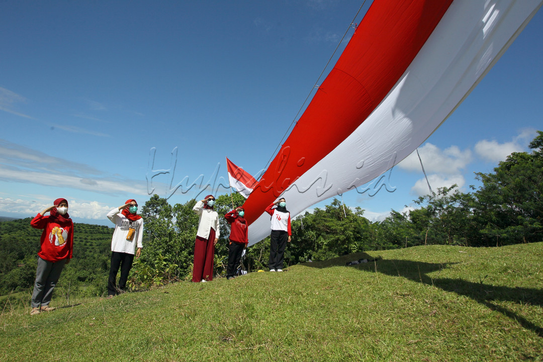 Sejumlah remaja memberi penghormatan kepada bendera Merah Putih berukuran panjang 76 meter dengan lebar 2,5 meter yang dibentangkan di Bukit Teletubies di Desa Kamiri, Luwu Utara, Sulsel, 17 Agustus 2021, dengan tetap menjaga jarak dan memakai masker. 