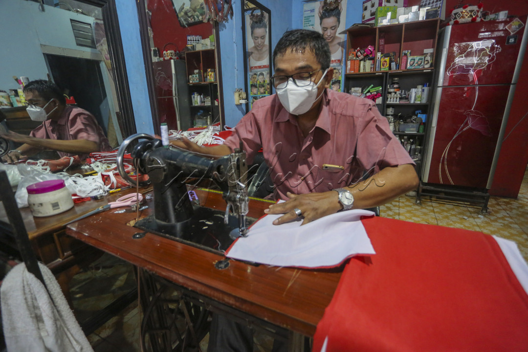Seorang Bapak sedang menjahit Bendera Merah Putih dijual untuk pengahasil tambahan , di massa PPKM saat ini menjual bendera Merah Putih saat merayakan hari Kemerdekaan Republik Indonesia moment yang baik untuk menambah penghasilan buat keluarga.