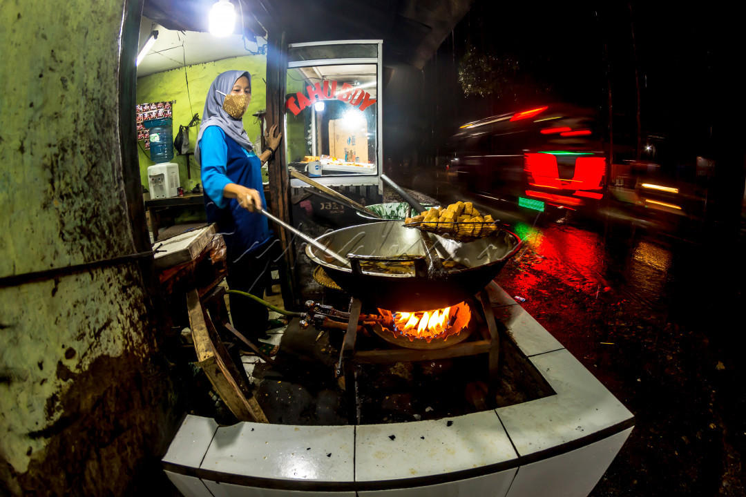 Seorang pedagang tahu di wilayah Sumedang, Jawa Barat terlihat tetap berjualan di malam hari pada saat pandemi ini dengan prokes tentunya
