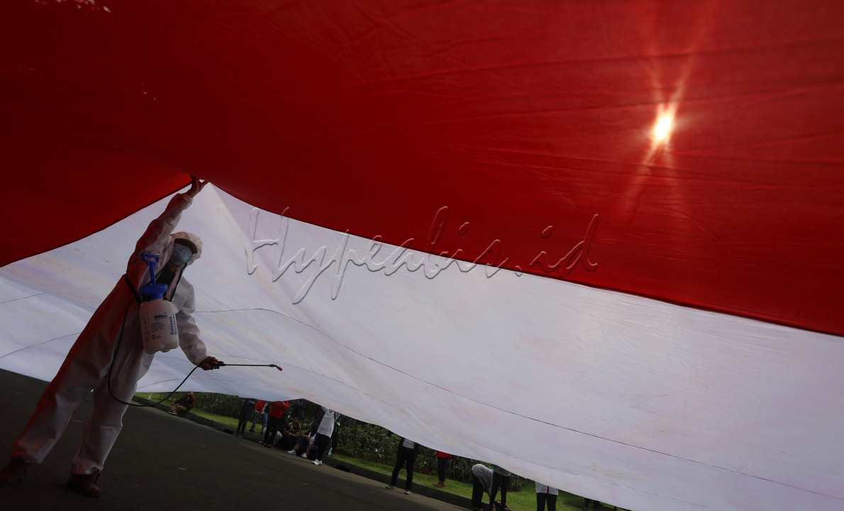 Petugas dengan menggunakan pakaian hazmat melakukan penyemprotan disinfektan saat sejumlah aktivis mengibarkan bendera Merah Putih raksasa di kawasan silang Monas, Jalan Medan Merdeka Barat, Jakarta, Rabu (2/6/2021). Bendera raksasa berukuran 1.200 meter persegi dikibarkan untuk memperingati bulan Pancasila dan peran Bung Karno yang menjadi simbol ideologi negara, untuk merajut kembali nasionalisme dan patriotisme yang terkoyak.