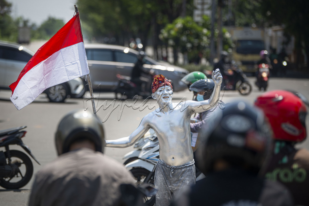 Pengamen 'manusia silver' membawa bendera merah putih saat beraksi di salah satu persimpangan jalan di Sunter, Jakarta, Kamis (12/8/2021). Sejumlah pengamen 'manusia silver' setempat juga menggunakan pernak-pernik merah putih, seperti bendera dan ikat kepala untuk memeriahkan hari ulang tahun (HUT) ke-76 Republik Indonesia. 