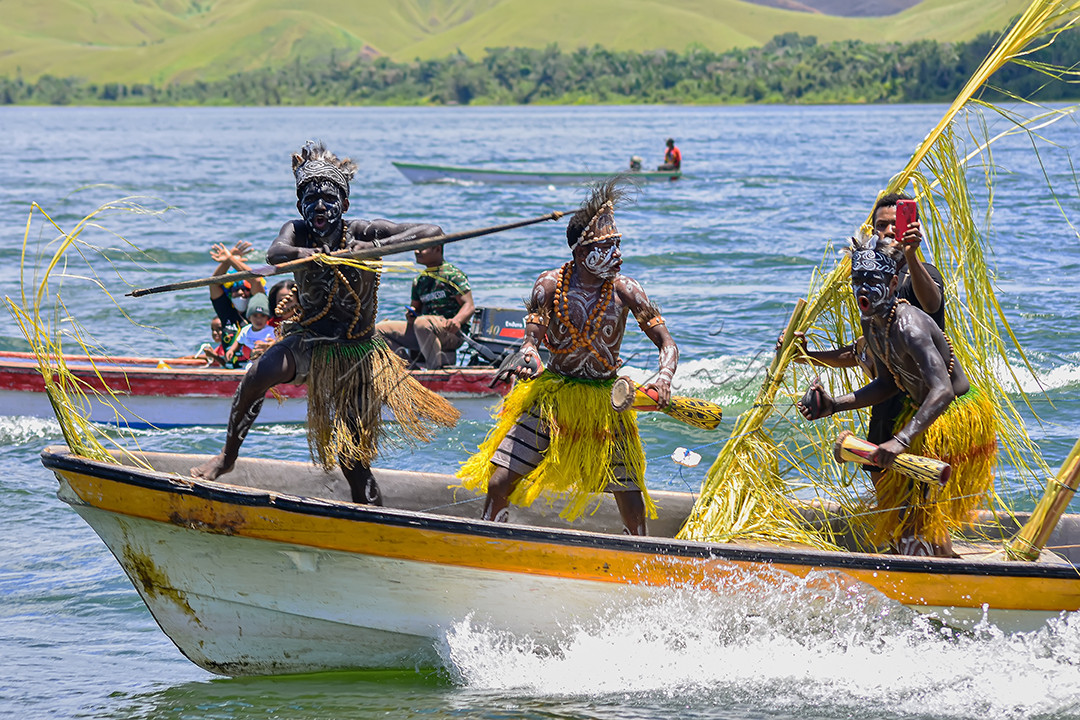Di dalam foto ini, dapat kita lihat bagaimana kentalnya budaya masyarakat sentani, papua. nampak kedua Pria berpakaian adat itu menari tarian adat mereka diatas speedboat, di tengah-tengah luasnya dan keindahan alam yang asri di danau sentani, Papua.