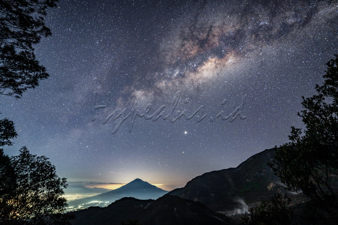 Milky Way atau Bima Sakti menghiasi langit malam di Kawasan Taman Wisata Alam Gunung Papandayan, Kabupaten Garut. Fenomena alam yang indah ini seringkali menjadi buruan para pecinta fotografi landskap dihampir seluruh negara di dunia tak terkecuali di Indonesia. Walaupun belakangan fenomena ini sedikit sulit untuk dilihat karena makin banyaknya penyebaran polusi cahaya yang terjadi. Namun dibeberapa tempat kita masih mungkin untuk menyaksikannya secara langsung. Salah satunya di Ghober Hoet, Gunung Papandayan ini. Ghober Hoet sendiri menjadi salah satu spot terbaik yang layak dikunjungi jika ingin mencoba memotret Milky Way. Dengan tambahan latar belakang Gunung Cikuray yang begitu unik karena berbentuk segitiga raksasa, makin membuat potret yang kita ambil bisa lebih menarik. Waktu terbaik untuk memotret Milky Way ini sendiri biasanya terjadi pada bulan April-September saat langit malam sedang cerah-cerahnya. 