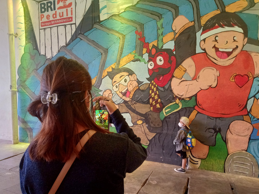 Seorang ibu sedang memotret anaknya dengan background mural di terowongan kendal, Sudirman (28/05/2022).