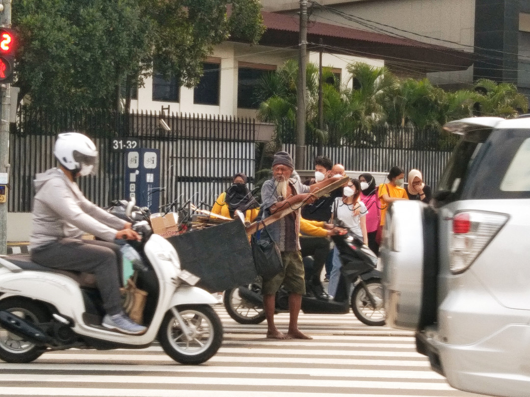 Seorang bapak yang menarik gerobaknya ingin menyeberang jalan, tampak di sisi kanan (pengguna motor) dan kirinya (pengguna mobil). Walaupun berbeda keadaan sosialnya, tetapi mereka tetap berada di jalan yang sama Indonesia. Jakarta, Rabu (27/07/22).