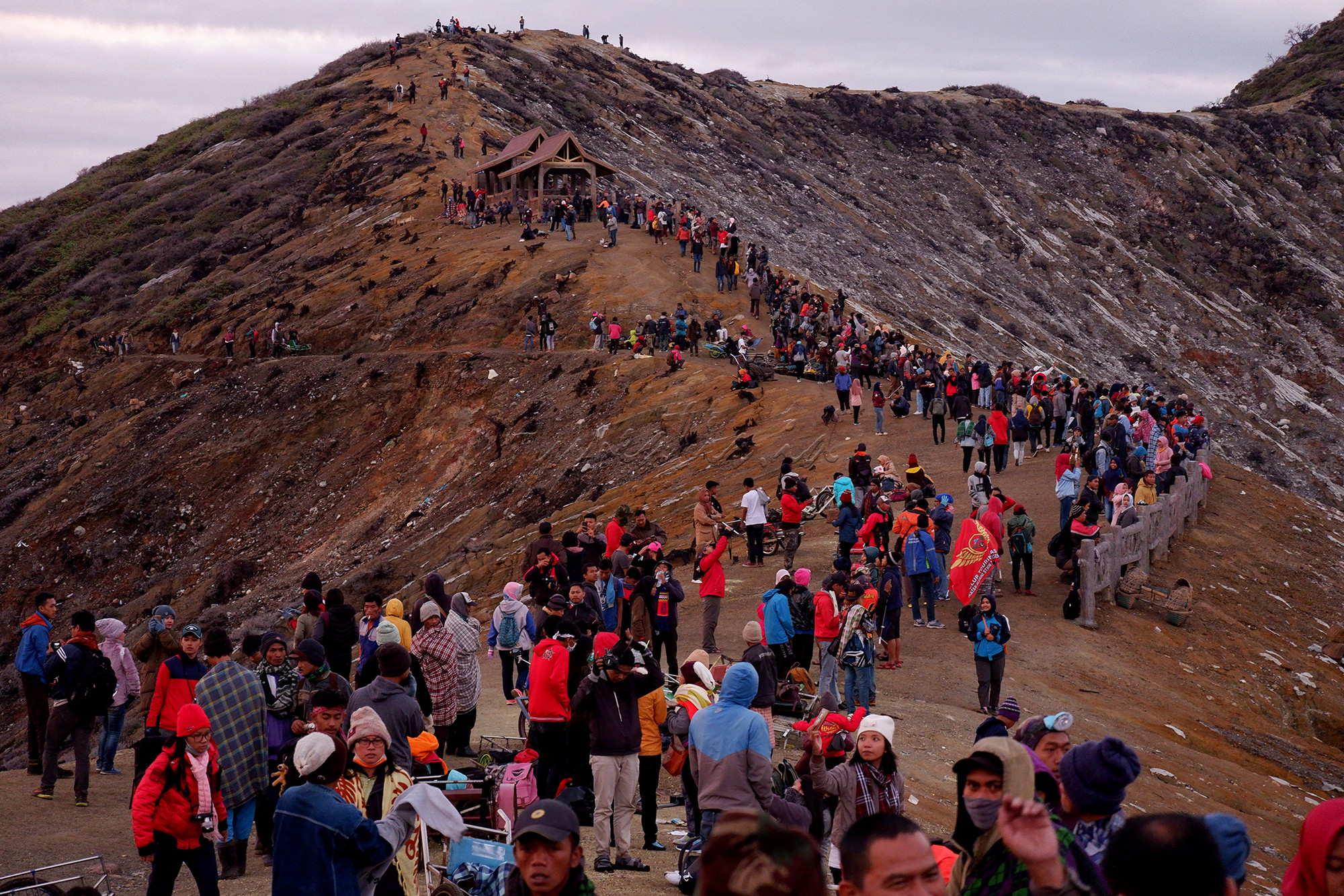 Wisatawan menikmati pagi di kawasan puncak Gunung Ijen, Bondowoso, Jawa Timur. Gunung Ijen berada di kawasan Wisata Kawah Ijen dan Cagar Alam Taman Wisata Ijen dan masih menjadi destinasi wisata populer dan unggulan di Jawa Timur. Kawah Ijen berada di ketinggian 2.368 meter di atas permukaan laut (mdpl). Kawah berdinding kaldera setinggi 300-500m, luasnya sekitar 5.466 hektar. Kawah ini terletak di tengah kaldera terluas di Pulau Jawa. Ukuran kaldera sekitar 20 kilometer. Ukuran kawahnya sekitar 960 meter x 600 meter. Kawah berada di kedalaman lebih dari 300 meter di bawah dinding kaldera. Air kawah itu cukup tenang dan berwarna hijau kebiru-biruan.